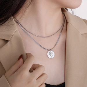 Dettaglio di una collana a due strati in acciaio argento con ciondolo floreale inciso