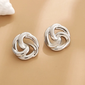 Detailed macro view of silver-plated geometric spiral knot earrings on warm beige background