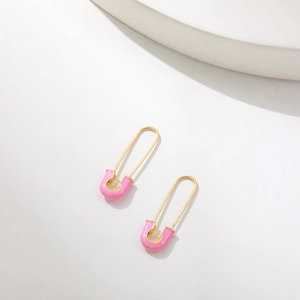 Detail of gold safety pin earrings with vibrant pink enamel finish on white background