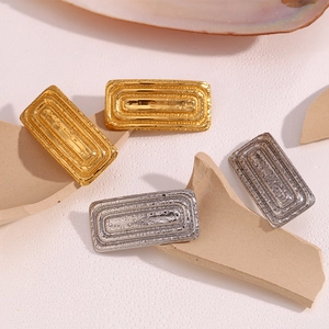 Macro shot of rectangular textured earrings in gold and silver on minimalist ceramic