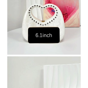 White acrylic heart-shaped handbag with rhinestone handle shown next to 6.1-inch phone
