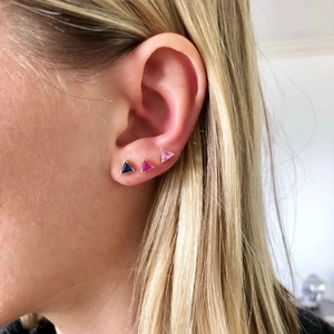 Detailed close-up of three triangle cartilage studs in blue and pink on ear