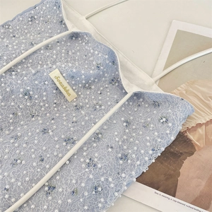 Detailed view of light blue bag featuring white lace mesh, pearls, and floral embroidery