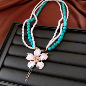 Detail of multi-layer pearl necklace with green beads and white enamel flower pendant