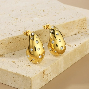 Macro detail of gold teardrop earrings with pavé zircons on a textured stone stand