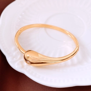 Detailed view of a gold teardrop bangle with embedded cubic zirconia on a ceramic plate