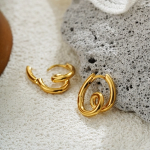 Macro shot of twisted irregular 18K gold earrings on a natural grey rock texture