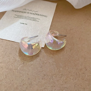 Macro shot of iridescent acrylic C-shape hoop earrings on a textured brown background