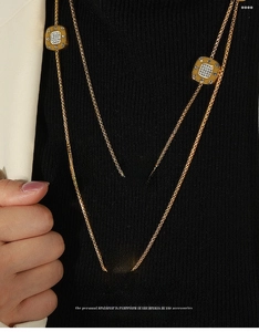 Detail of gold box chain necklace with hollow geometric square pendants on black sweater