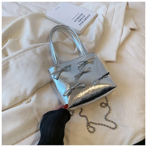 Close-up of silver metallic handbag featuring small bow decorations and a sleek chain strap