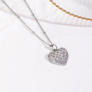 Macro detail of silver heart pendant with woven texture and clear crystals on bead chain