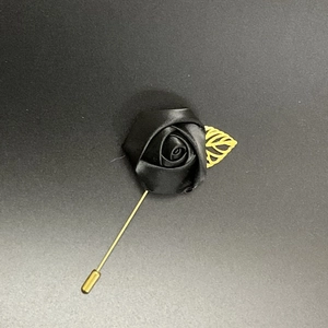 Detail of a handmade black satin rose lapel pin with a delicate golden leaf and long needle