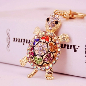 Cartoon turtle keychain with colorful rhinestones on a golden metal shell, close-up view