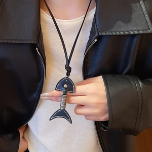 Close-up of a vintage leather fishbone pendant necklace worn over a black leather jacket