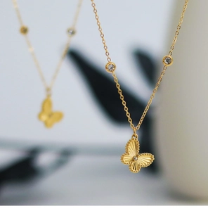 Detail of gold butterfly pendant with textured wings and zircon stones on a chain