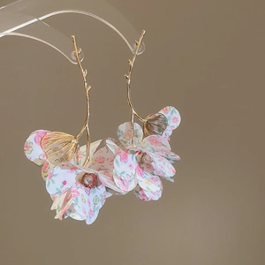 Detailed close-up of golden branch earrings with delicate pink fabric petals