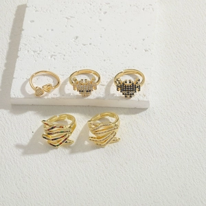 Detailed view of five gold-tone geometric rings with colorful zircon on a textured stone