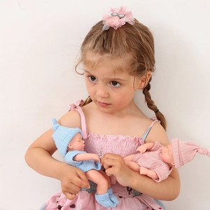 Girl holding two mini 20cm reborn baby dolls in blue and pink knitted outfits