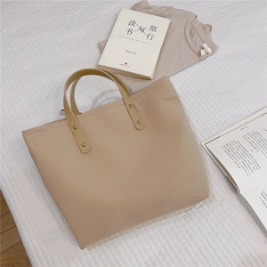 Detail of minimalist beige tote bag with brown leather handles on a waffle bedspread