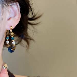 Close-up of drop earrings with tiger eye, blue beads, and white pearls on a model