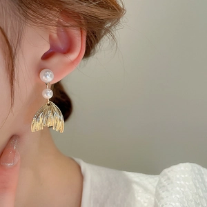 Close-up of golden fishtail earrings with white pearls worn by a model in soft light