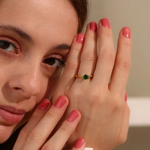 Détail d'une bague chaîne plaquée or 18K avec une pierre verte sur le doigt d'une femme