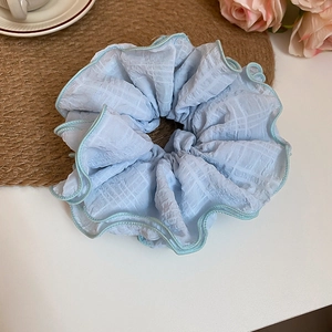 Detail of light blue plaid fabric scrunchie with ruffled edges and soft texture