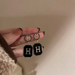 Close-up of gold-plated black enamel earrings with letter H detail held by a hand