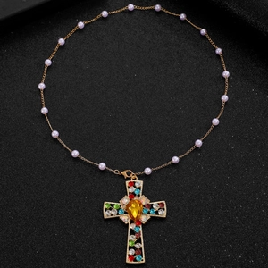 Detailed close-up of golden cross pendant with colorful rhinestones and purple beads