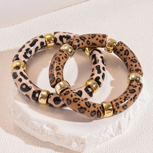 Acrylic leopard print bangle bracelets with gold metal beads on a stone pedestal