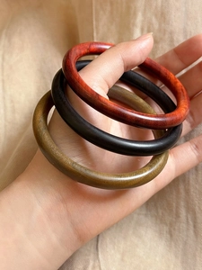 Vue détaillée de trois joncs circulaires en bois en rouge, noir et vert olive à grain naturel