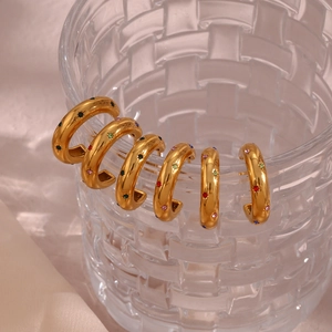 Set di sei orecchini a cerchio dorati con strass colorati appesi su un vetro