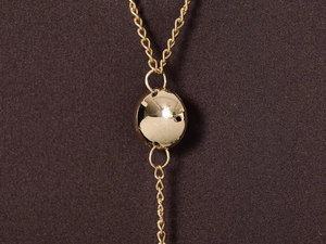 Macro detail of a polished gold ball pendant on a fine link chain with knit fabric background