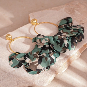 Macro shot of gold hoop earrings with camouflage fabric ruffles on a beige stone slab