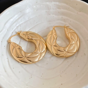 Detail of gold hoop earrings with star geometric engraving in a ceramic bowl