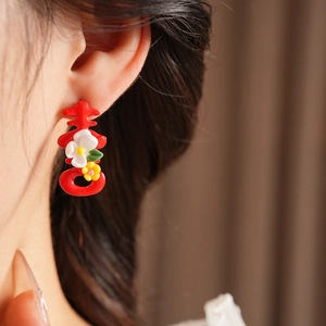 Close-up of red 'Xi' character earrings with small floral accents on a model's ear