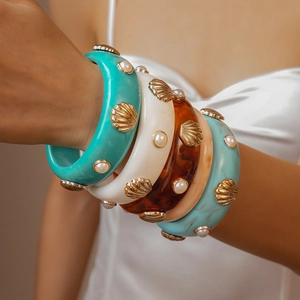 Détail macro de larges bracelets en résine avec coquillages dorés et perles