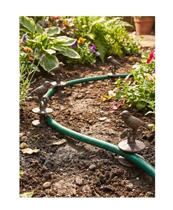 Close-up of a vintage cast iron bird garden hose guide stake set among green plants