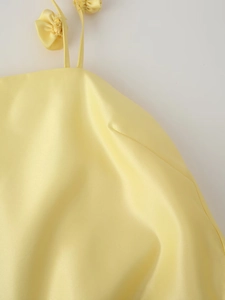 Detail of yellow satin dress featuring 3D floral strap and glossy fabric texture