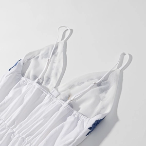Detail of white cotton dress showing thin straps and intricate blue floral embroidery