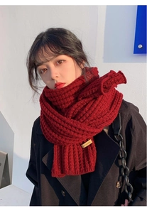 Detail of red chunky knit scarf with a handmade leather tag on a female model