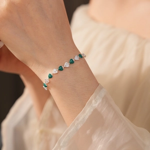 Close-up of heart charm bracelet with green enamel and white zircons on female wrist