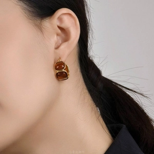 Detail view of oval amber resin earrings with 18K gold plating on a fashion model