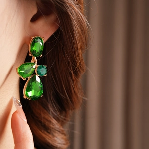 Detailed view of vintage gold water drop earrings with green rhinestones worn by a model