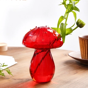 Detail shot of a red mushroom-shaped glass vase with water drops and green plant