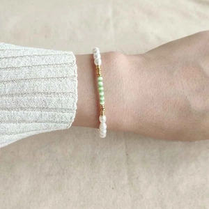 Detail of beaded bracelet with white pearls and mint green cat-eye stones on wrist