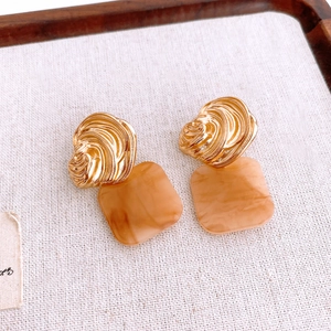 Detail of French luxury gold square earrings with amber marble acrylic pendants on linen