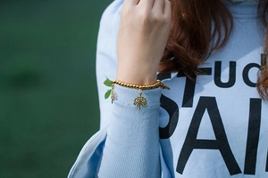 Détail d'un bracelet à billes dorées avec pendentifs Arbre de Vie porté par un mannequin