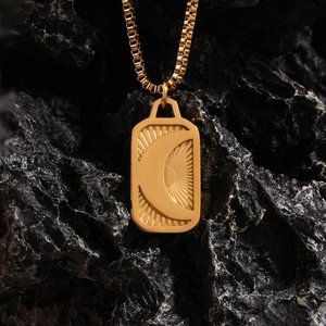 Macro detail of engraved moon pendant on 18K gold plated necklace over black rock