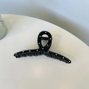 Detailed view of a large black hair claw clip with white polka dots on a white surface
